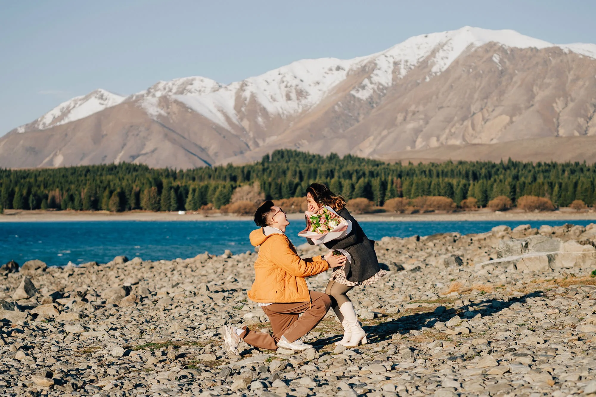 A couple just after a surprise proposal at Lake Tekapo with blue water in the background